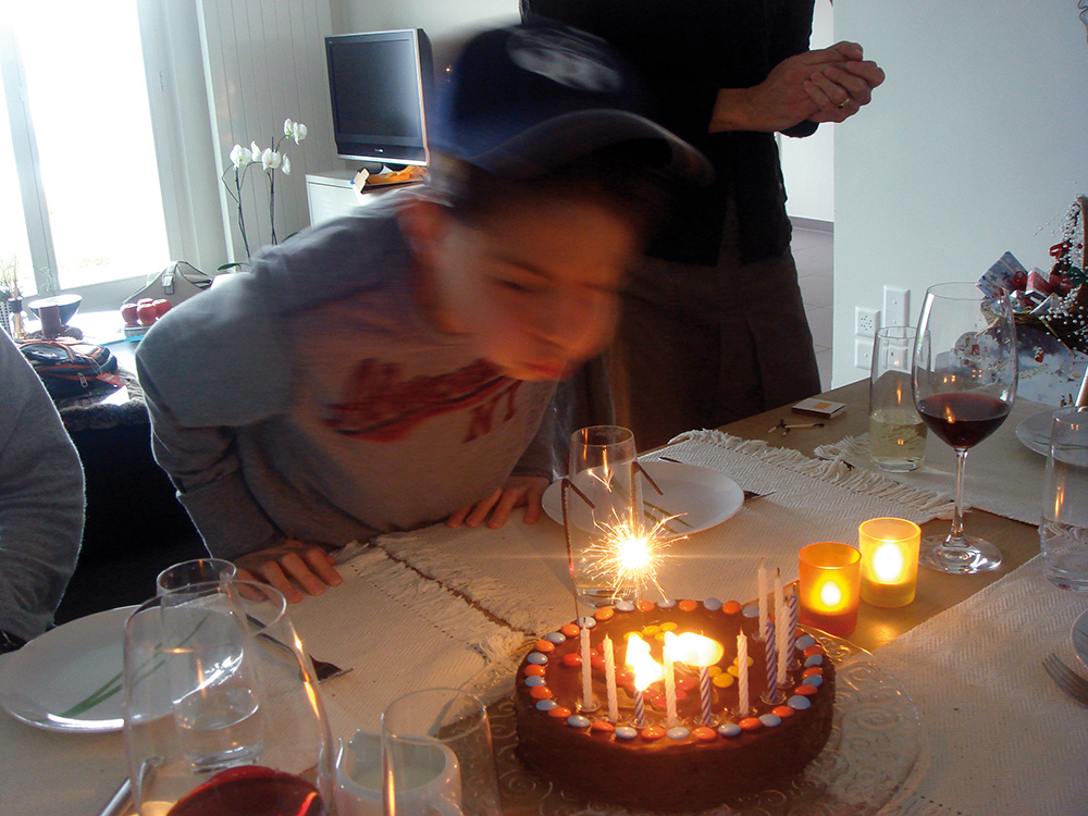 Junge bläst Kerze auf Geburtstagskuchen aus